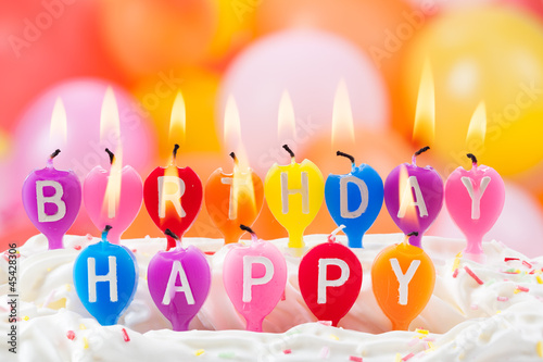 Photo: Happy Birthday written in lit candles on colorful background Happy Birthday written in lit candles on colorful background