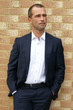 Smartly dressed man posing against a brick wall