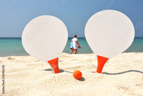 Photo: Two rackets and a ball on the sandy beach Two rackets and a ball on the sandy beach
