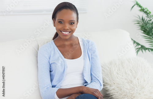 Photo: Black woman sitting on a sofa looking at camera Black woman sitting on a sofa looking at camera