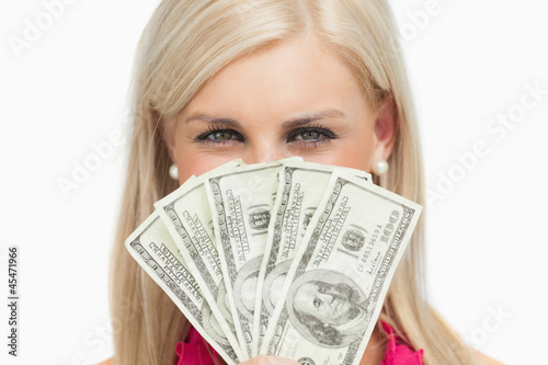 Photo: Smiling blonde hiding her face with 100 dollars banknotes Smiling blonde hiding her face with 100 dollars banknotes