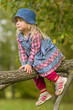 Adorable girl in dress and hat climb on tree near playground