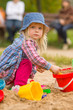 Photo: Adorable girl in dress and hat play on sandbox on playground Adorable girl in dress and hat play on sandbox on playground