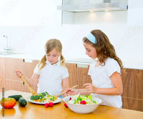 Photo: Beautiful chef sisters at home kitchen preparing salad Beautiful chef sisters at home kitchen preparing salad