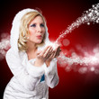 junge blonde Frau im Winteroutfit pustet Schnee