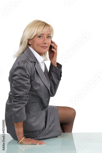 Photo: Senior businesswoman perched on desk during call Senior businesswoman perched on desk during call