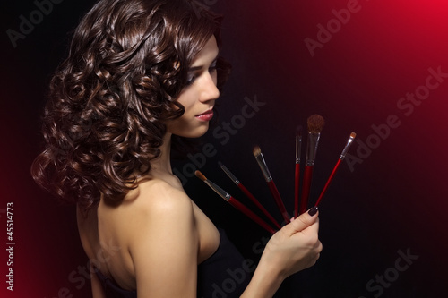 Photo: Beautiful girl with makeup brushes on black background Beautiful girl with makeup brushes on black background