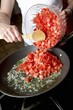 Woman Adding Fresh Diced Tomatoes into a Skillet on the Stove
