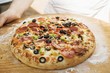 Hands holding pepperoni pizza with peppers and olives