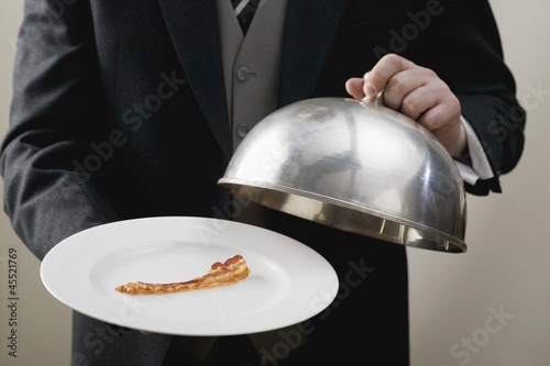 Photo: Butler serving rasher of fried bacon on plate with dome cover Butler serving rasher of fried bacon on plate with dome cover