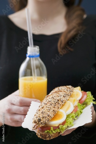 Photo: Woman holding sandwich and bottle of orange juice Woman holding sandwich and bottle of orange juice