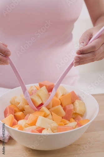 Photo: Woman taking fruit salad out of bowl with salad servers Woman taking fruit salad out of bowl with salad servers