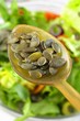 Pumpkin seeds on a spoon above a bowl of salad