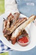 A person holding a plate of grilled spare ribs and barbecue sauce