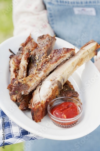 Photo: A person holding a plate of grilled spare ribs and barbecue sauce A person holding a plate of grilled spare ribs and barbecue sauce