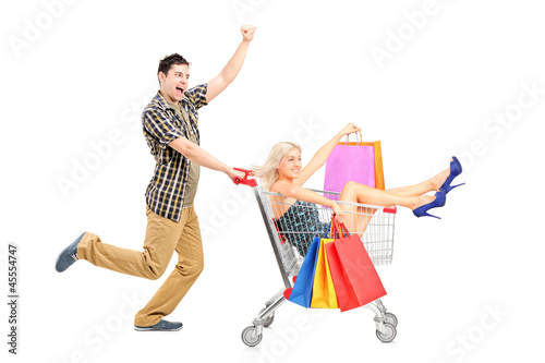Photo: Excited person pushing a smiling woman with bags in a shopping c Excited person pushing a smiling woman with bags in a shopping c