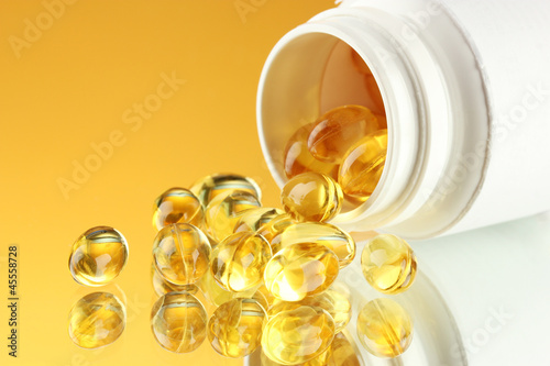 Photo: Capsules in bottle, on yellow background Capsules in bottle, on yellow background