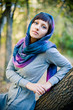 Foto: The girl in a scarf and in a knitted dress sits on a tree. The girl in a scarf and in a knitted dress sits on a tree.