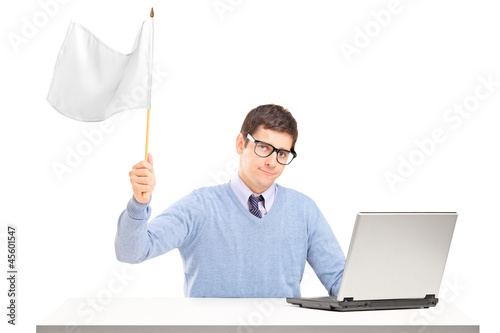 Photo: Sad man sitting with laptop and holding a white flag gesturing d Sad man sitting with laptop and holding a white flag gesturing d