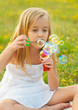Cute little girl blowing soap bubbles and sitting on the meadow