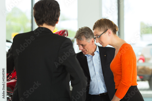 Photo: man with couple and auto in car dealership looking under hood man with couple and auto in car dealership looking under hood