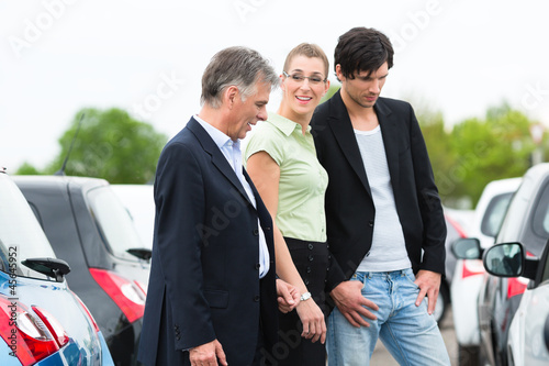 Photo: Couple looking at car on yard of dealer Couple looking at car on yard of dealer