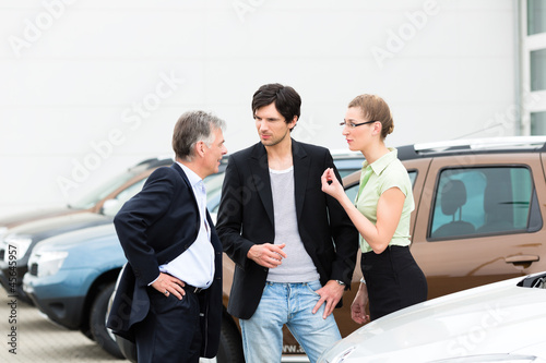 Photo: Couple looking at car on yard of dealer Couple looking at car on yard of dealer