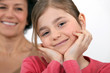 A little girl posing with her mother in the background.