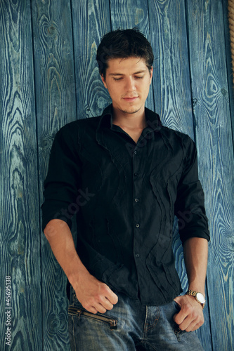 Photo: Handsome man casually leaning against the wooden board wall Handsome man casually leaning against the wooden board wall