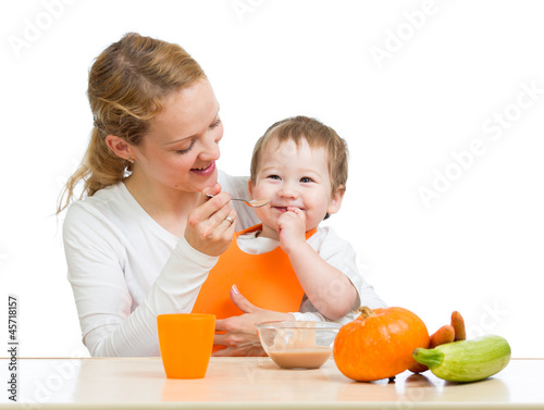 Photo: young mother spoon feeding her baby boy isolated on white young mother spoon feeding her baby boy isolated on white