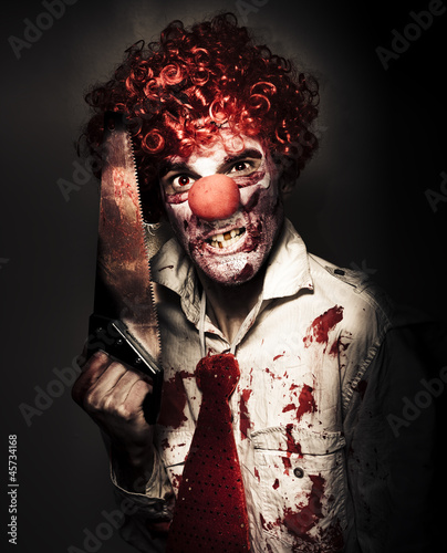 Photo: Angry Horror Clown Holding Butcher Saw In Darkness Angry Horror Clown Holding Butcher Saw In Darkness