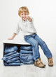 Child on cardboard box packed with jeans. Showing thumbs up