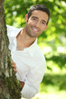 Peekaboo. Man in a white shirt peering round a tree.