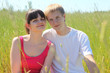 Husband, wife seat on long grass in field