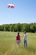 Wife, husband launch kite in field near wood, back