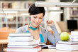 Woman with green apple surrounded with piles of books reads