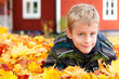 Blonder kleiner Junge im Herbstlaub vor Holzhaus in Schweden
