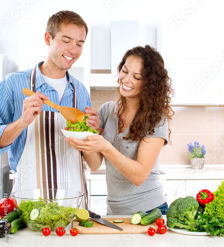 Photo: Young Man Cooking. Happy Couple Eating Fresh Vegetable Salad Young Man Cooking. Happy Couple Eating Fresh Vegetable Salad