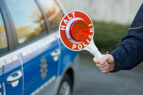 Photo: Polizist hält Polizeikelle vor Polizeiauto Polizist hält Polizeikelle vor Polizeiauto