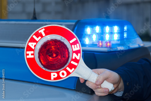 Photo: Polizist hält Polizeikelle vor Polizeiauto Polizist hält Polizeikelle vor Polizeiauto