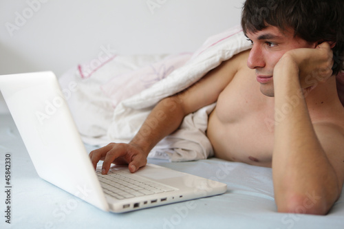 Photo: junger mann mit laptop im bett junger mann mit laptop im bett