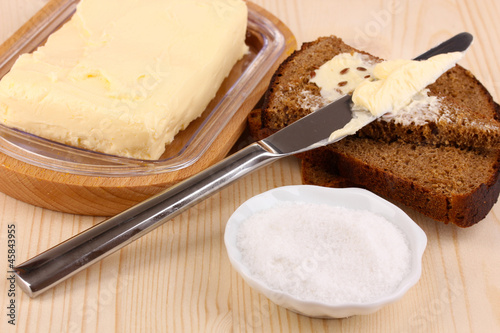 Photo: Butter on wooden holder and bread on wooden table close-up Butter on wooden holder and bread on wooden table close-up