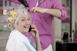 A senior woman on a mobile phone whilst having her hair dried