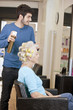 A male hairdresser applying hairspray to a female clients hair