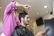 Man looking at a digital tablet whilst having his hair cut