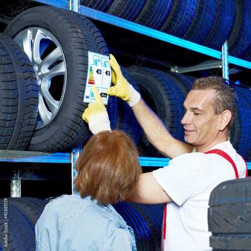 Photo: Motor mechanic explains tire labeling to a customer in a garage Motor mechanic explains tire labeling to a customer in a garage