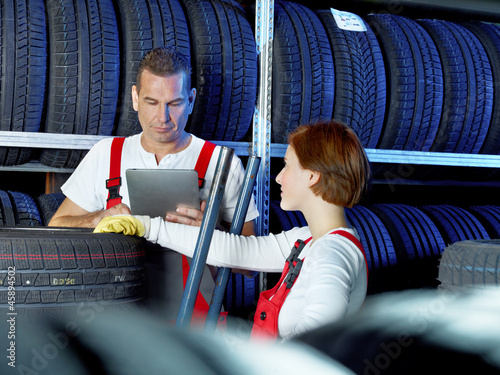 Photo: Car mechanics work in a warehouse for tires with touchpad Car mechanics work in a warehouse for tires with touchpad