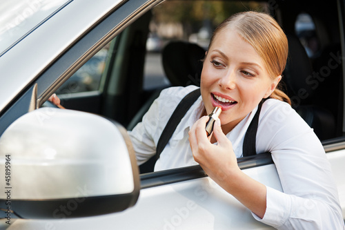 Photo: female painting her lips and driving the car female painting her lips and driving the car