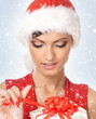 Portrait of a young woman in a Santa hat opening a present