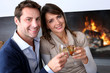 Cheerful couple drinking champaign by fireplace